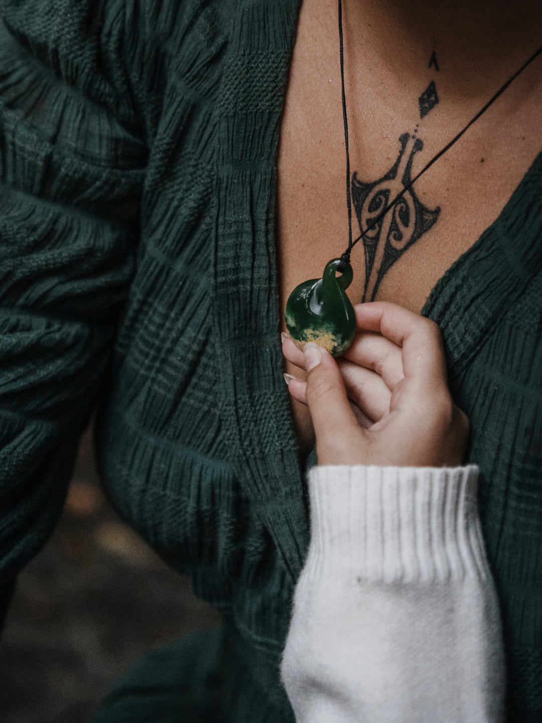 A child's hand holding onto a pikorua pendant that's worn by a woman around her neck